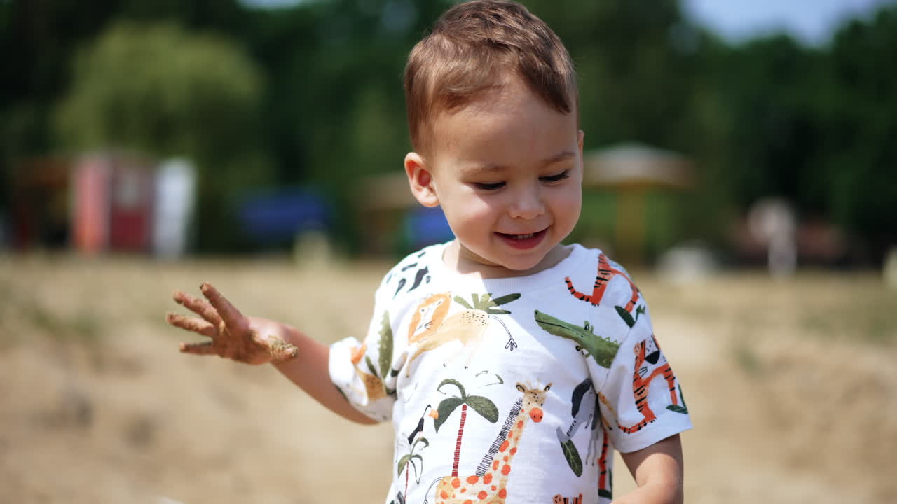 Happy kid plays with sand on the shore. Baby boy throws the sand and runs up to camera.