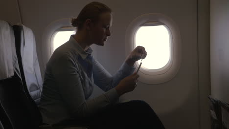 in airplane view of woman making payment with bank card using smartphone and dongle for scanning bank card