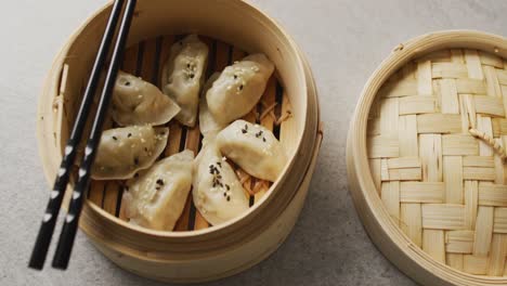 Composition-of-bamboo-steamer-with-gyoza-dumplings-and-chopsticks-on-grey-background