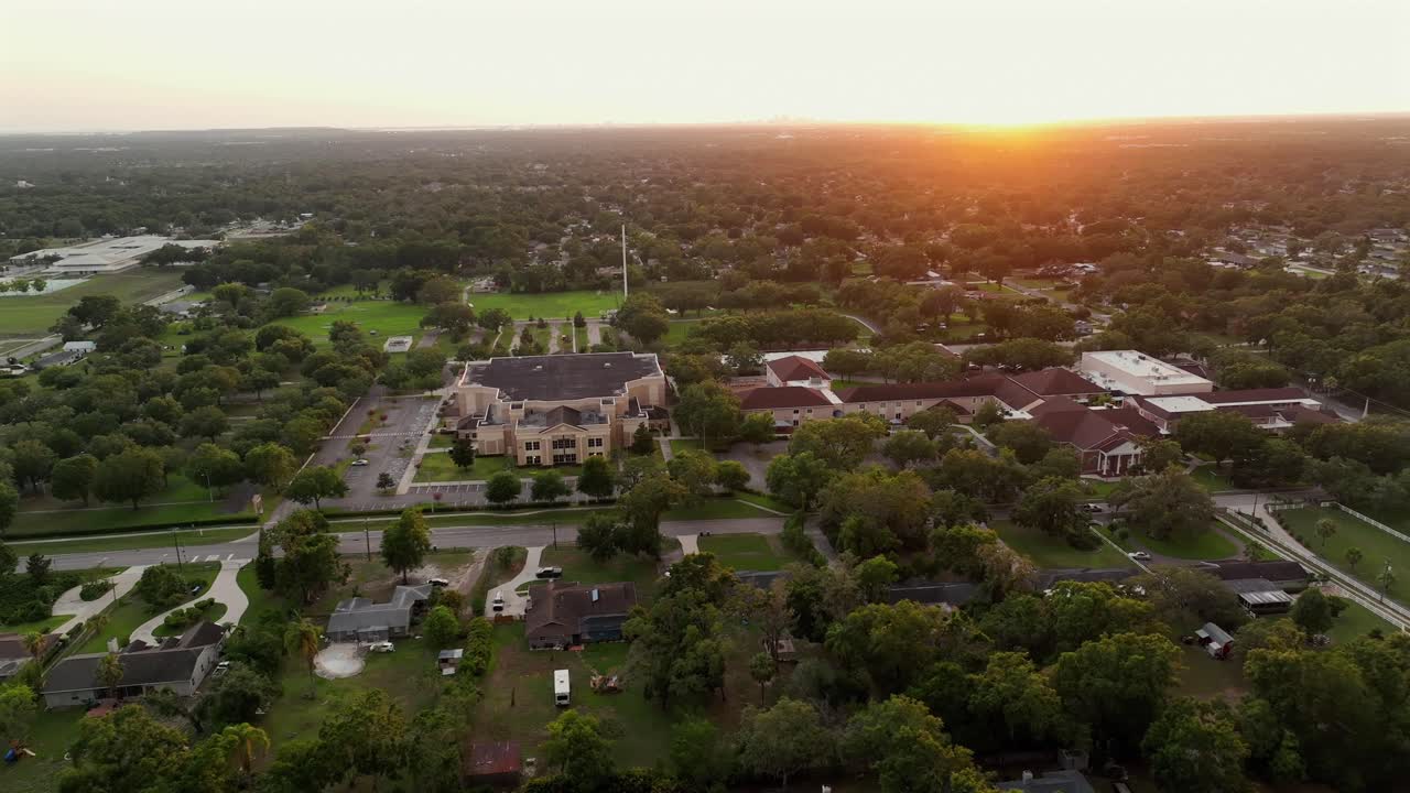 Cars on main street of luxury american town with Bell Shoals Church in Brandon while golden sunset. Aerial wide shot. Green trees in tropical suburb of Florida State, United States.