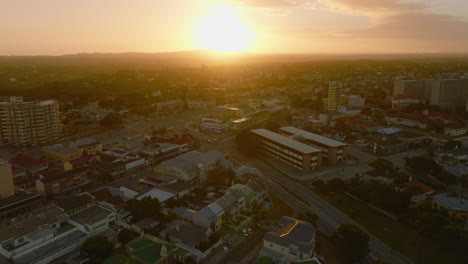 Forwards-fly-above-large-town,-streets-and-buildings-against-golden-sunset-sky.-Port-Elisabeth,-South-Africa