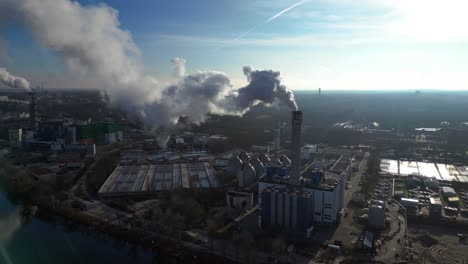Waste to energy plant emitting smoke from its chimney, located near an urban area, environmental impact of waste. Wonderful aerial view flight rotation to left drone