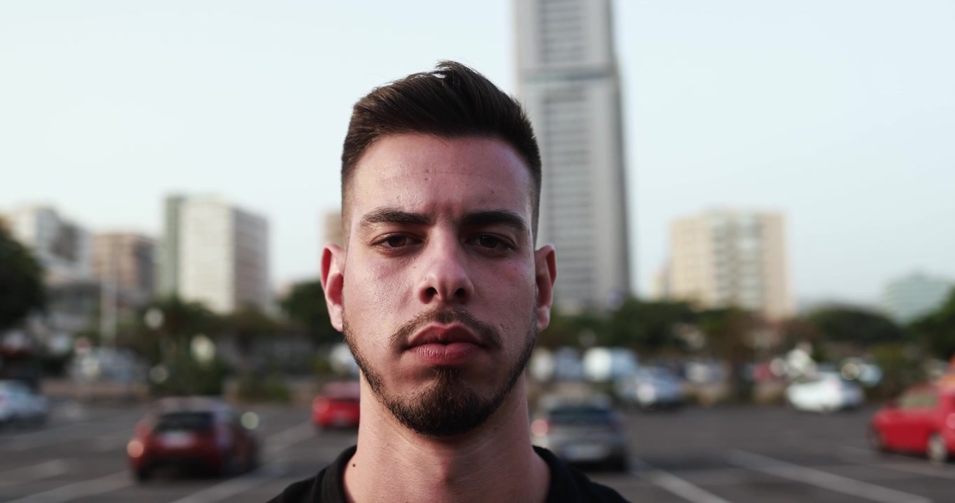 Primo piano di un giovane uomo serio che guarda in macchina in un contesto urbano