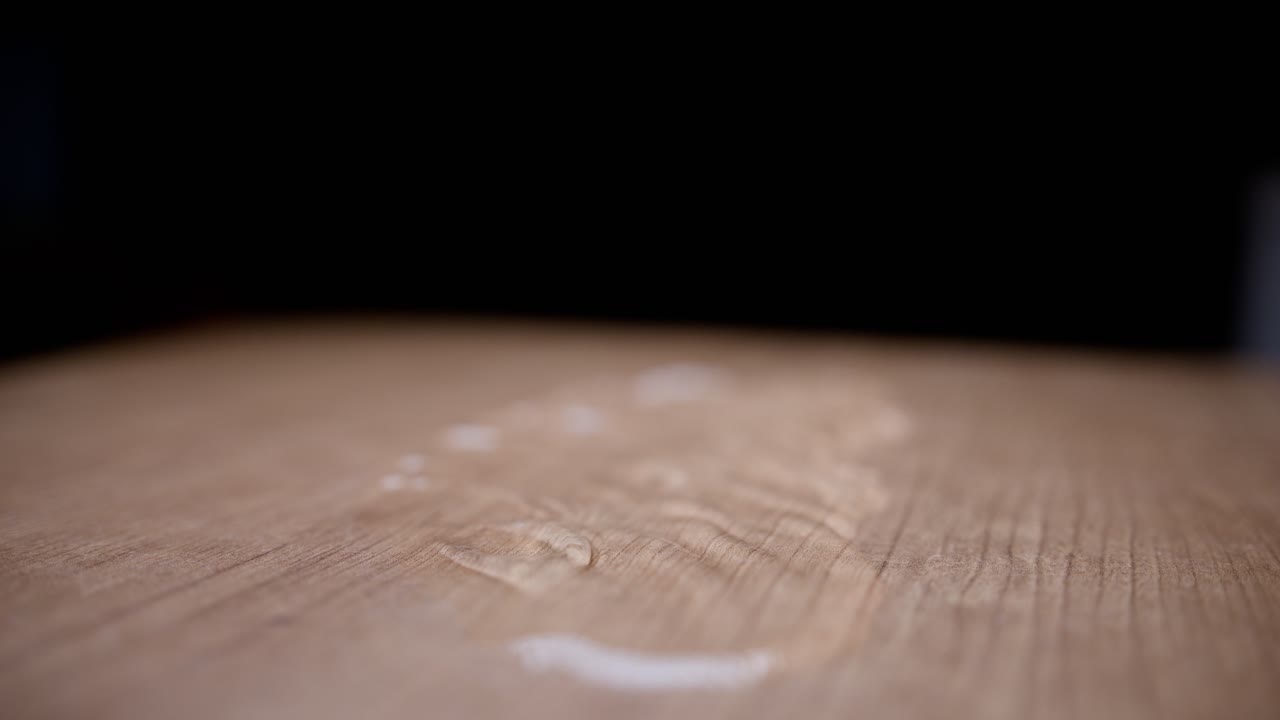 Water droplets falling onto a wooden surface in super slow motion, with a blurred background