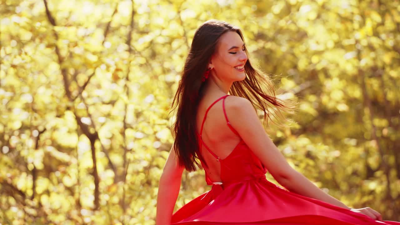 A Young Woman Gracefully Twirls in a Vibrant Red Dress Amidst a Lush Autumn Landscape, Radiating Joy and Elegance in the Sunshine