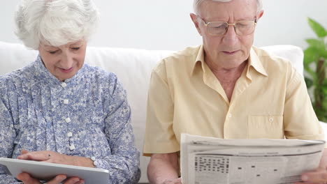 una pareja de ancianos usando un periódico y una tableta.