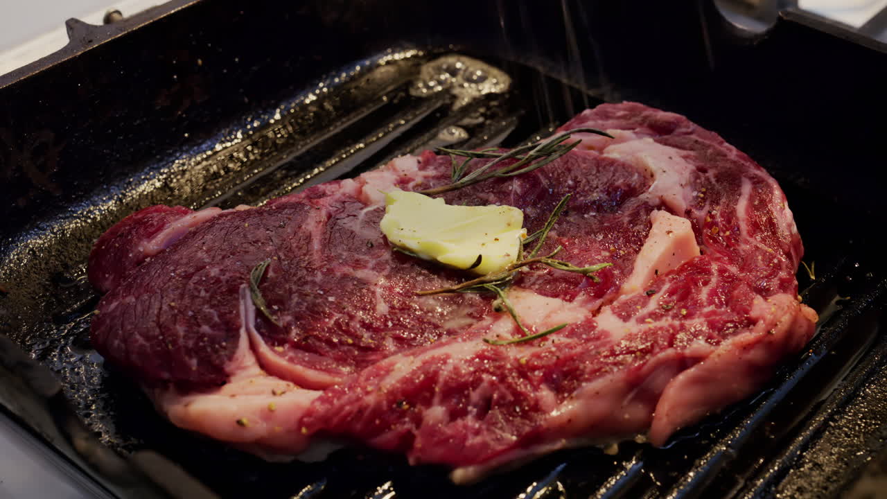Burro che si scioglie su una bistecca condita che cuoce su una padella griglia calda con rosmarino