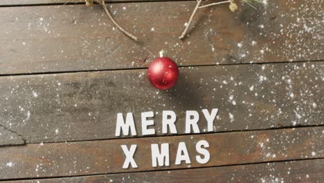 video of christmas greetings text and bauble decoration on wooden background