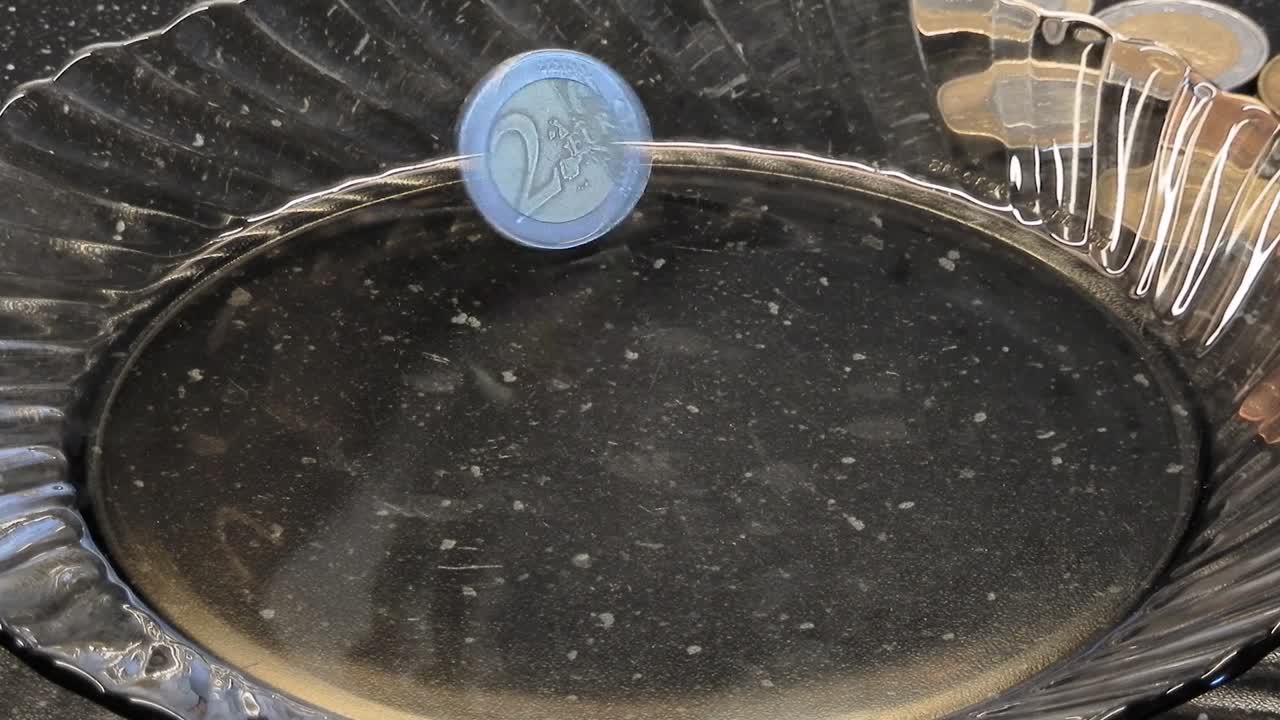 4k 영상 30fps 2 유로 동전 일어서서 유리 접시에 미친 것처럼 휘어지기 시작합니다.