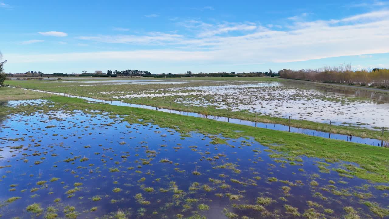 Aerial view of flooded fields in Christchurch, showcasing waterlogged landscapes under clear blue skies