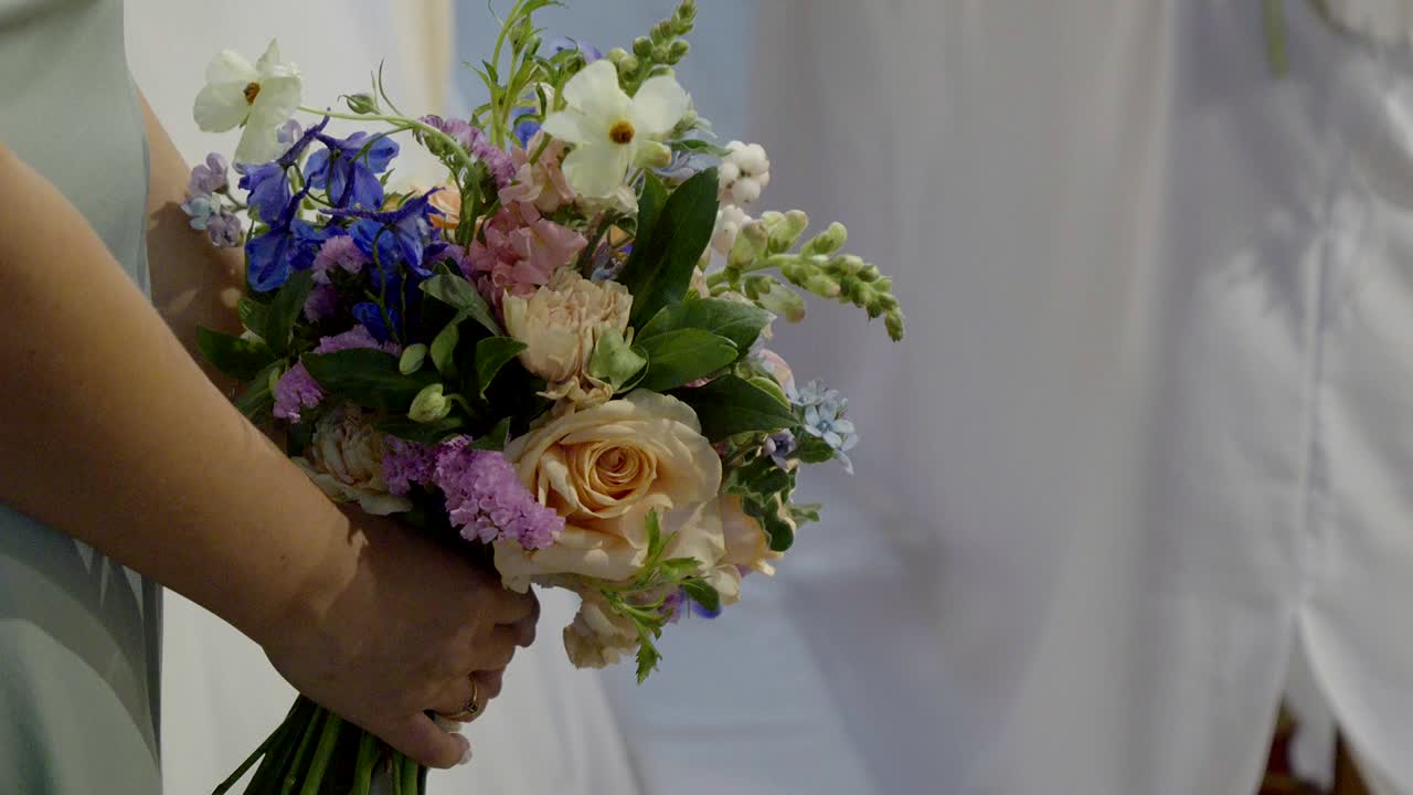 Primo piano di una damigella d'onore che tiene un bouquet nuziale in chiesa