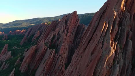 Aerial orbit ascend sunlit jagged red rocks and lush summer landscape, Arrowhead golf course Colorado