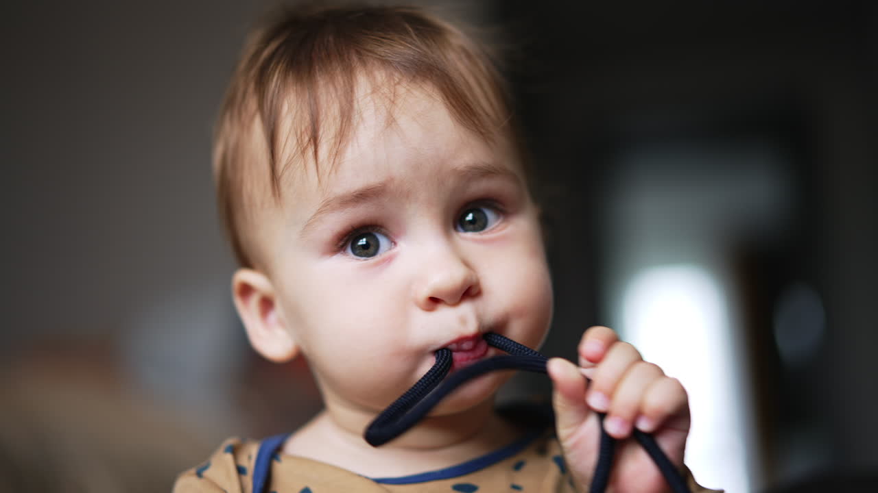 Cute funny baby boy holding a black cord in his mouth. Beautiful adorable kid portrait busy with a thing from the surrounding area. Close up.