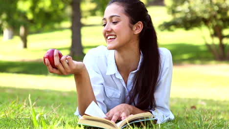 una chica bonita acostada en la hierba leyendo un libro