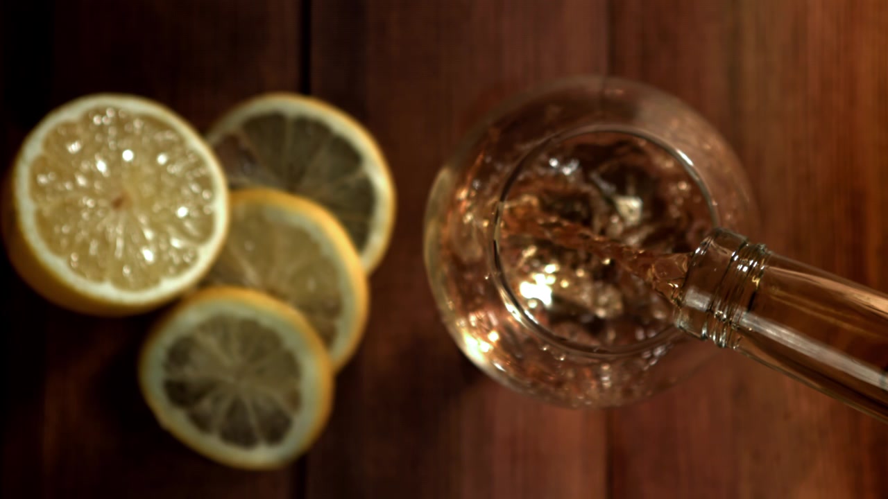 Versamento al rallentatore di bevanda dorata in un bicchiere con fette di limone