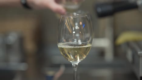 the male hands pouring bottle of white wine-champagne into transparent, clean round glass on the resraurant table in blurred close-up concept