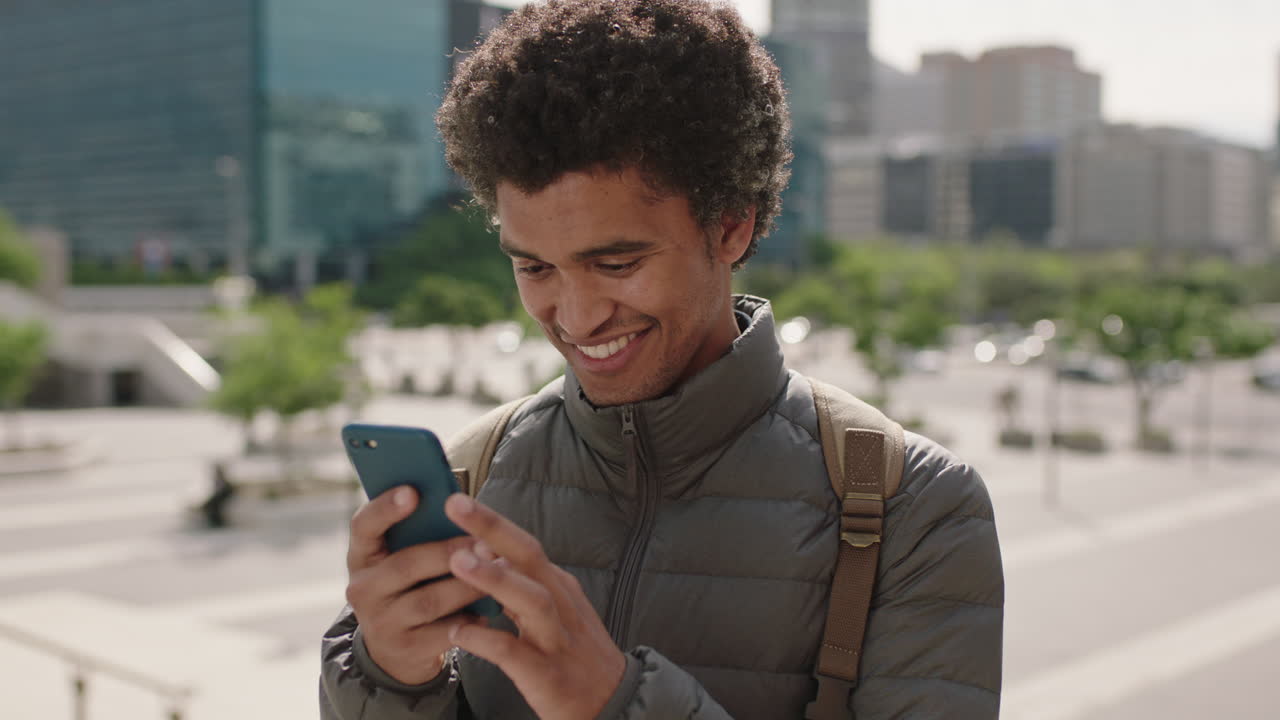 portrait of handsome young mixed race man enjoying browsing texting using smartphone social media app in sunny urban city background