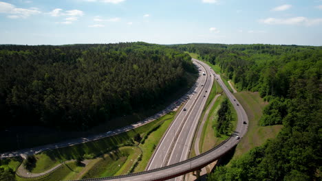 Ascending-aerial-view-of-cars-driving-on-new-asphalt-route-surrounded-by-forest-in-summer---4K-Drone-panorama