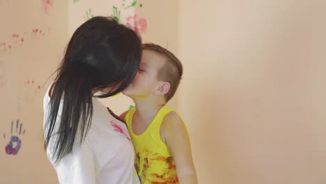 madre joven sosteniendo a su hijo en sus brazos, divirtiéndose, bailando después de dejar sus coloridas huellas de manos en la pared. cámara lenta