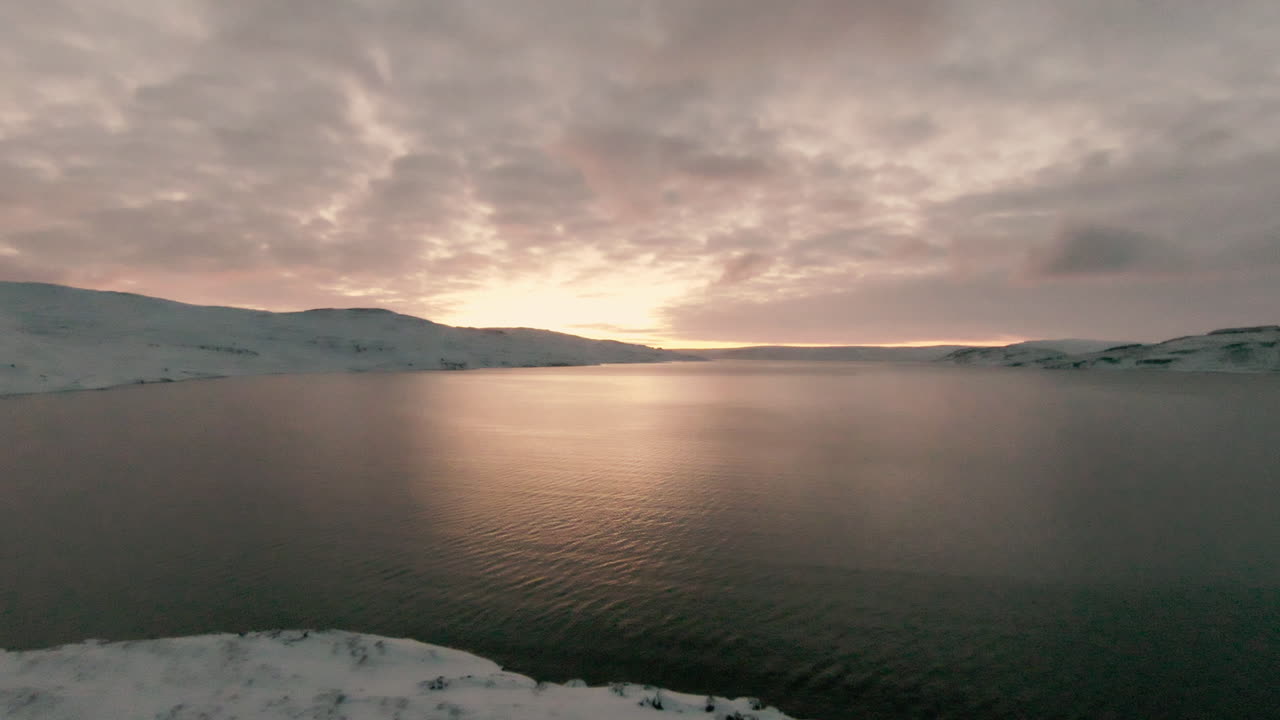 Dolly forward towards bright sunrise above ocean in winter landscape