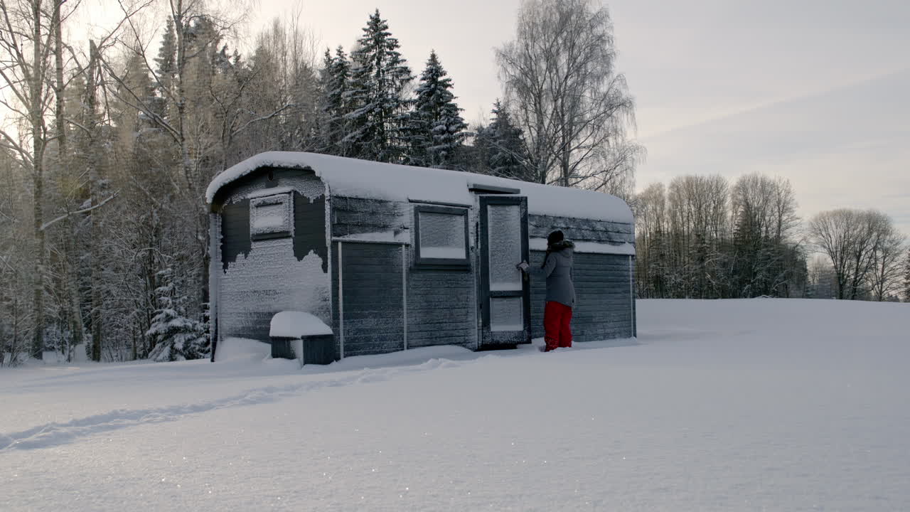Eine Person öffnet die Tür einer kleinen Holzhütte, um sich im kalten Winter aufzuwärmen.