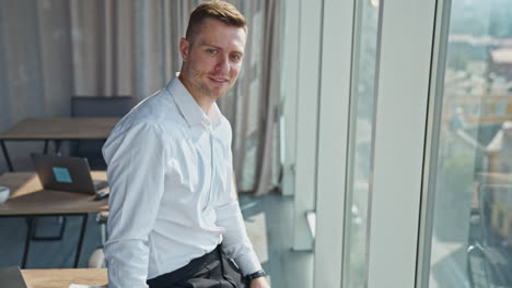 calm confident young businessman in white shirt standing at the window. man looks into sunlit window and then to the camera.