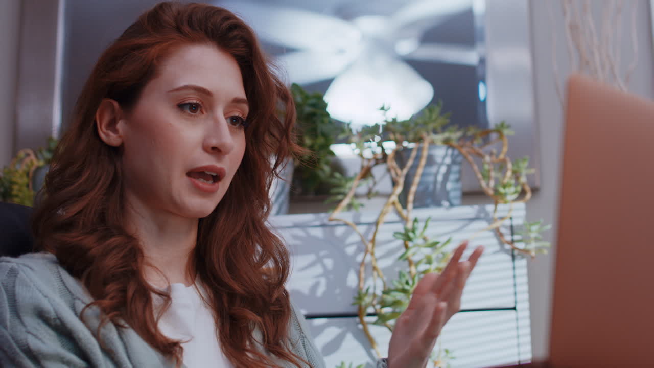 una joven mujer caucásica está trabajando desde casa en su computadora portátil, hablando en una videollamada