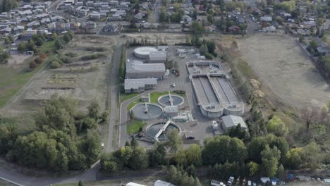 Aerial-backward-movement-shot-of-waste-water-treatment-plant-for-filtration-of-dirty-or-sewage-water-on-the-outskirts-of-a-town-on-a-bright-sunny-day