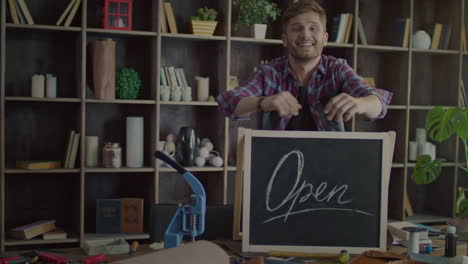 Happy-business-owner-putting-open-sign-on-table-in-small-shop