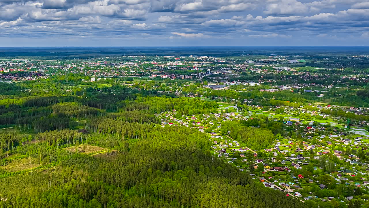 Clouds casting shadows on green forest near city in Latvia, aerial time lapse view