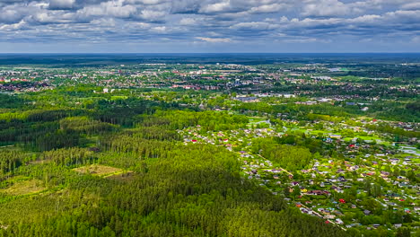 clouds casting shadows on green forest near city in latvia, aerial time lapse view