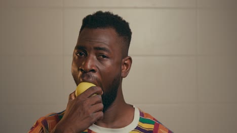 joven afroamericano barbudo mordiendo lentamente una manzana amarilla