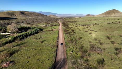 aerial shot of car on dirt road in willcox, arizona, wide tracking drone shot with mountains in the background with dust trails