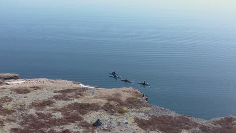 kayakers paddling along cliff shore of iceland in waveless fjord, aerial