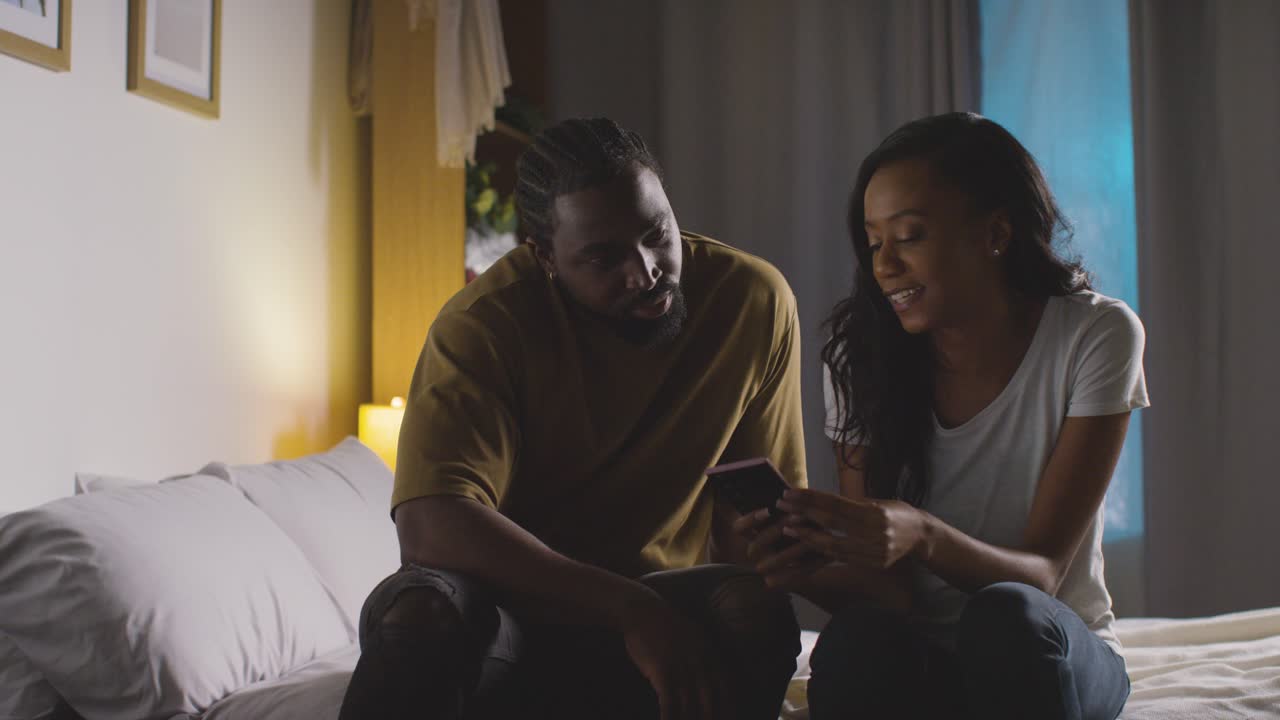 Young Couple Relaxing At Home At Night In Bedroom Looking At Mobile Phone Together 5