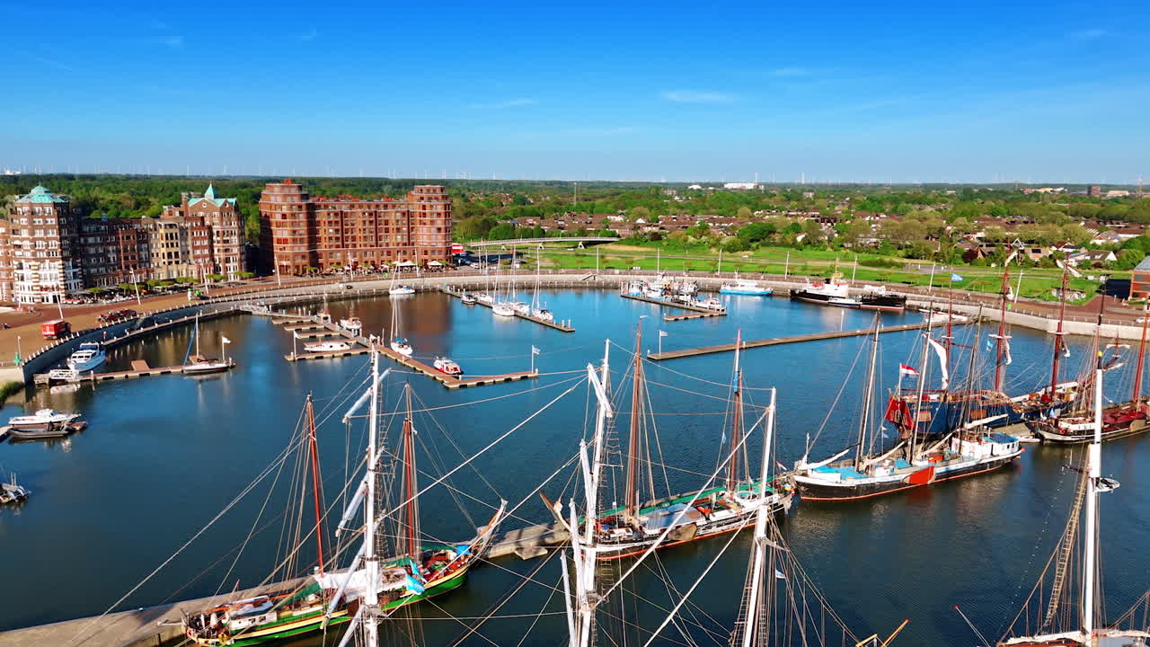 Beautiful ships with their sails down stand on the anchor near the berth. Approaching port of Lelystad, the Netherlands with stunning buildings at the waterfront.
