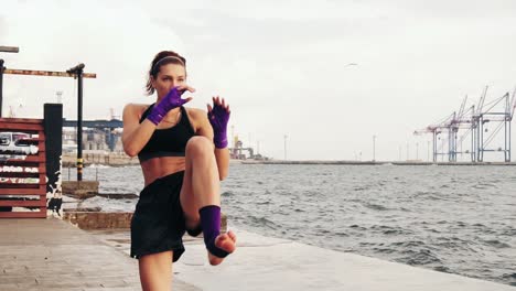 Young-female-boxer-practising-sidekick-of-her-legs-by-the-sea-in-slow-motion.-Beautiful-female-boxer-training-on-the-beach-in