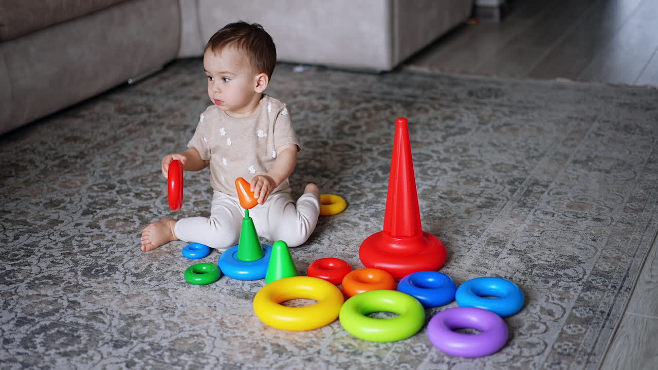 Peaceful Caucasian toddler plays with pyramids on the floor. Baby learning shapes and colors playing. High angle view.