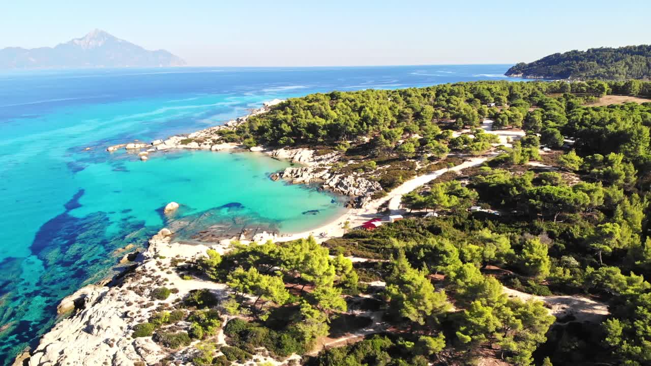 Aerial drone view of the Aegean sea rocky coast with blue transparent water, multiple greenery, mountain on the background. Greece