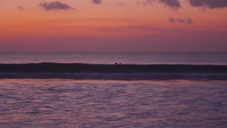 silhouetted couple enter sea water back lit with vivid colorful pink orange sunset sky during bali honeymoon, jimbaran