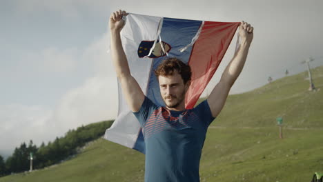 man holding a slovenian flag above his head to let it flutter in the wind