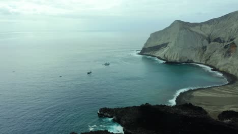 Dive-boats-and-steep-rocky-cliffs-drop-off-into-coastal-waters-on-overcast-day,-San-Benedicto-Revillagigedo-Islands-Mexico