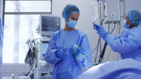 Diverse-female-surgeons-wearing-face-masks-and-protective-clothing-during-operation-in-hospital