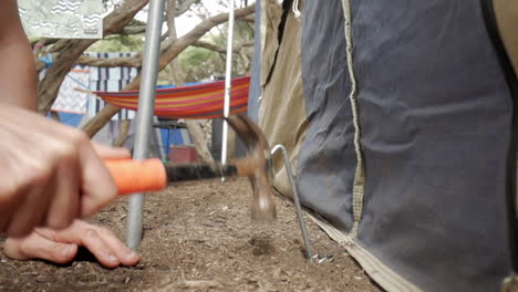 man hammers tent peg into the dirt or ground