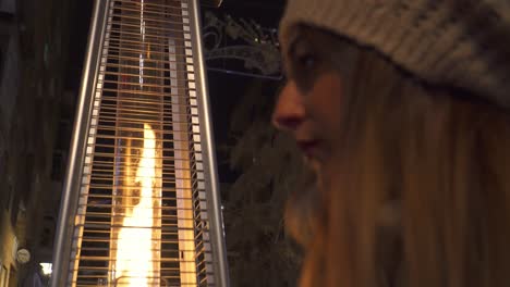 mujer con sombrero colocando su cabello junto a una estufa al aire libre que emite una llama de fuego y luz