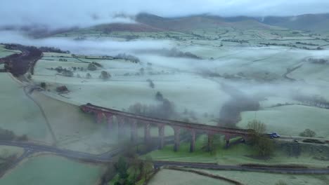 viaducto de piedra abandonado rodeado de colinas verdes al amanecer en invierno con niebla y baja cobertura de nubes