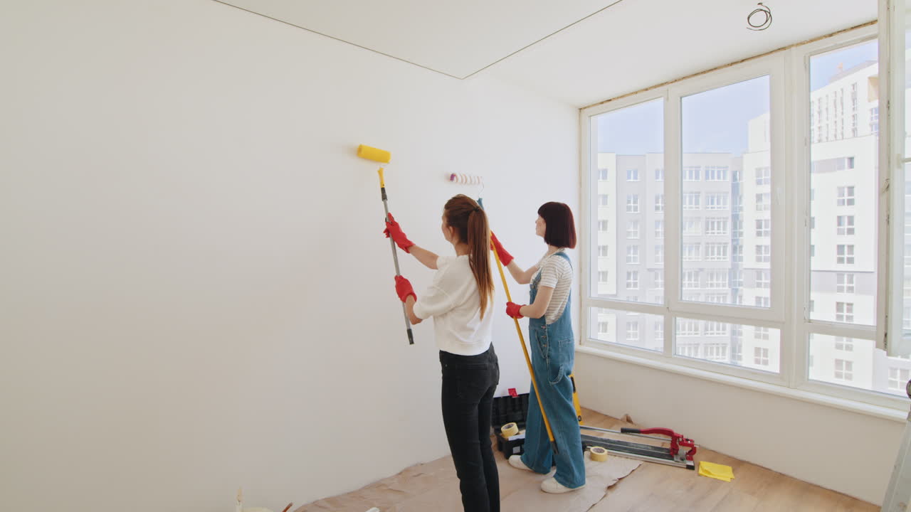 dos mujeres pintando una pared en una habitación en renovación