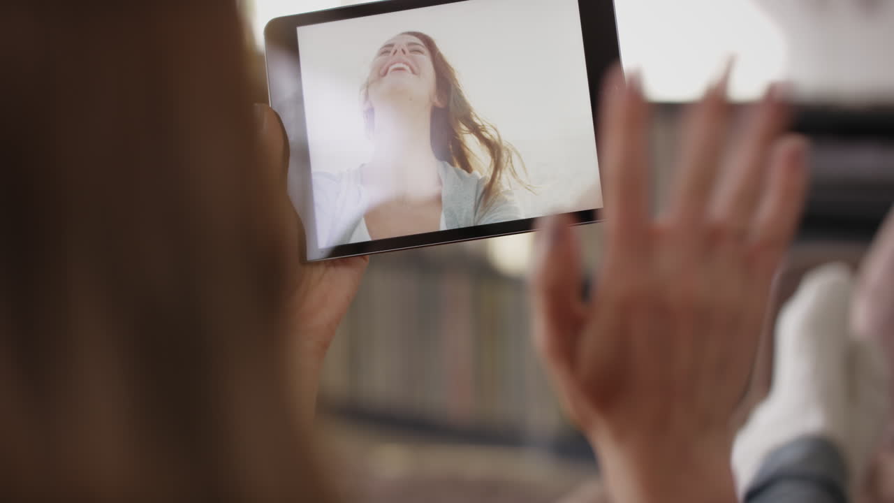 mujer saludando a un amigo de vacaciones en casa a través de un video de internet usando una aplicación de tableta digital en el sofá