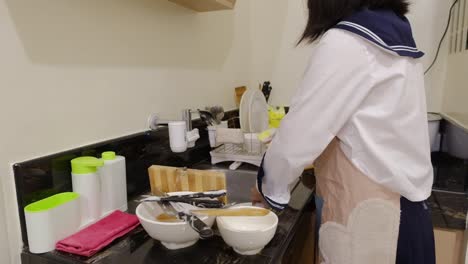 medium shot of a young, asian girl washing dishes and utensils in small kitchen