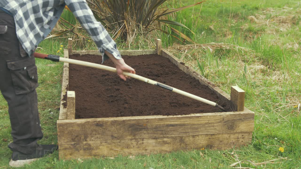 el hombre rastrillando abono en un jardín elevado para sembrar semillas y flores.